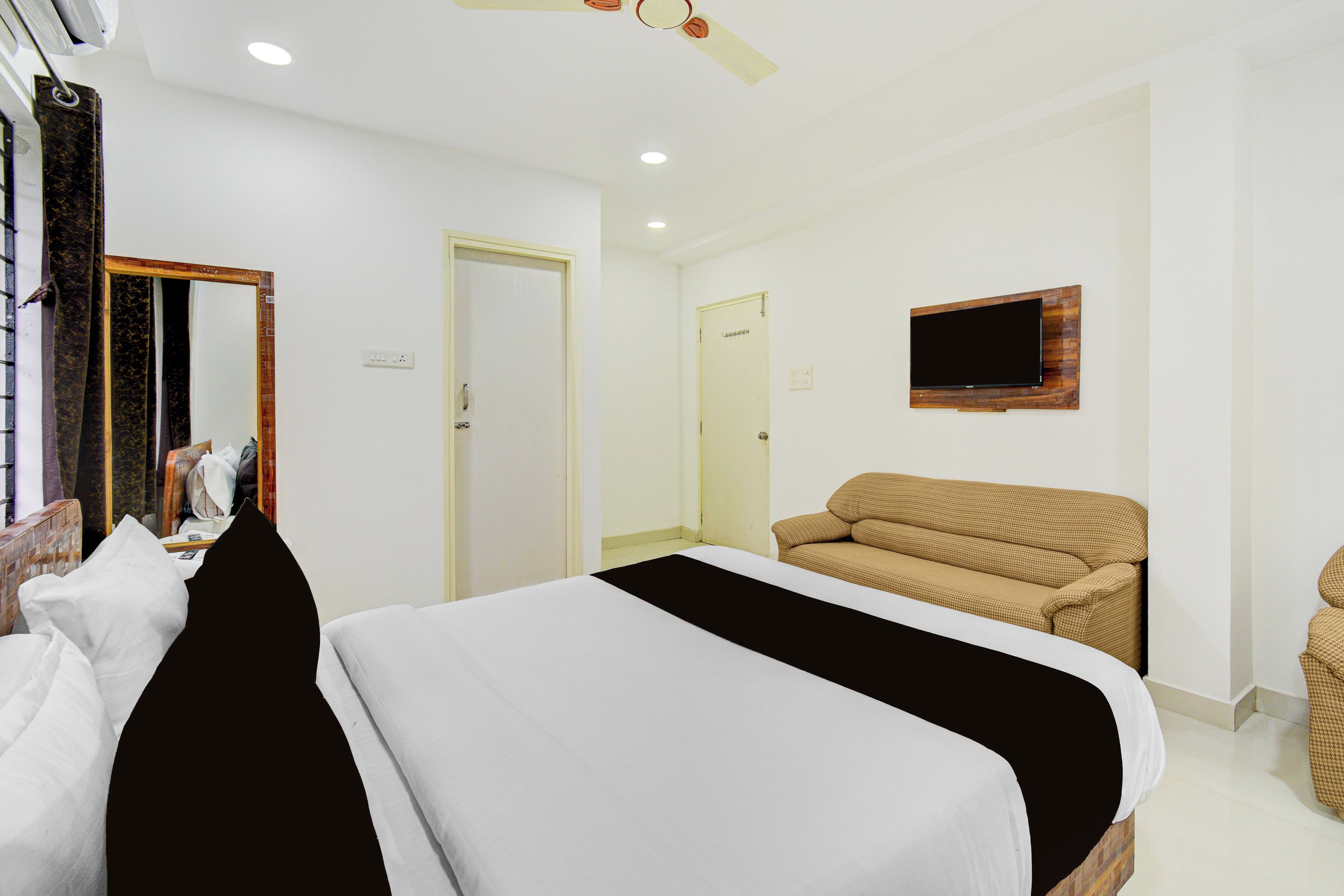 Una habitación de hotel con cama, sofá, televisión montada en la pared y ventilador de techo.