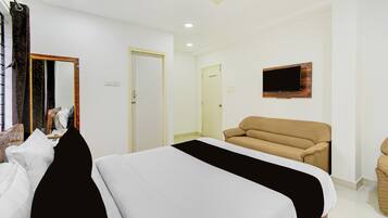 Una habitación de hotel con cama, sofá, televisión montada en la pared y ventilador de techo.