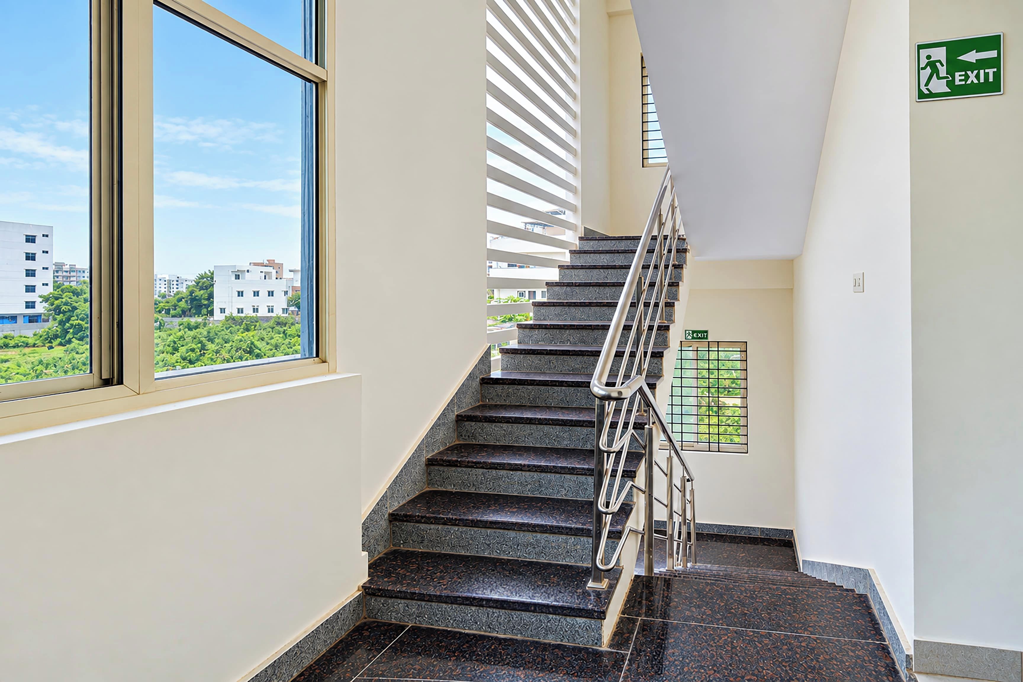 A staircase with a handrail, a window, and an exit sign.