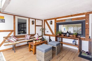 A cozy room with a wooden bench, a small table, wicker ottomans, and a television mounted on the wall. - Room 'Doppelzimmer 10' with Shared Garden and Wi-Fi (Stadtallendorf)