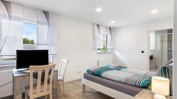 Ein Schlafzimmer mit einem Bett, einem Schreibtisch mit Computer, einem Stuhl und einem Fenster mit Vorhängen.