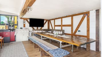 A dining area with a long wooden table, benches, and a television mounted on the wall.