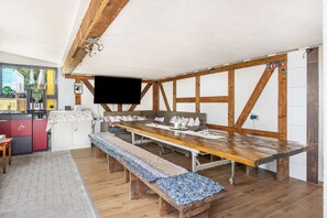Un espace repas avec une longue table en bois, des bancs et un téléviseur fixé au mur.