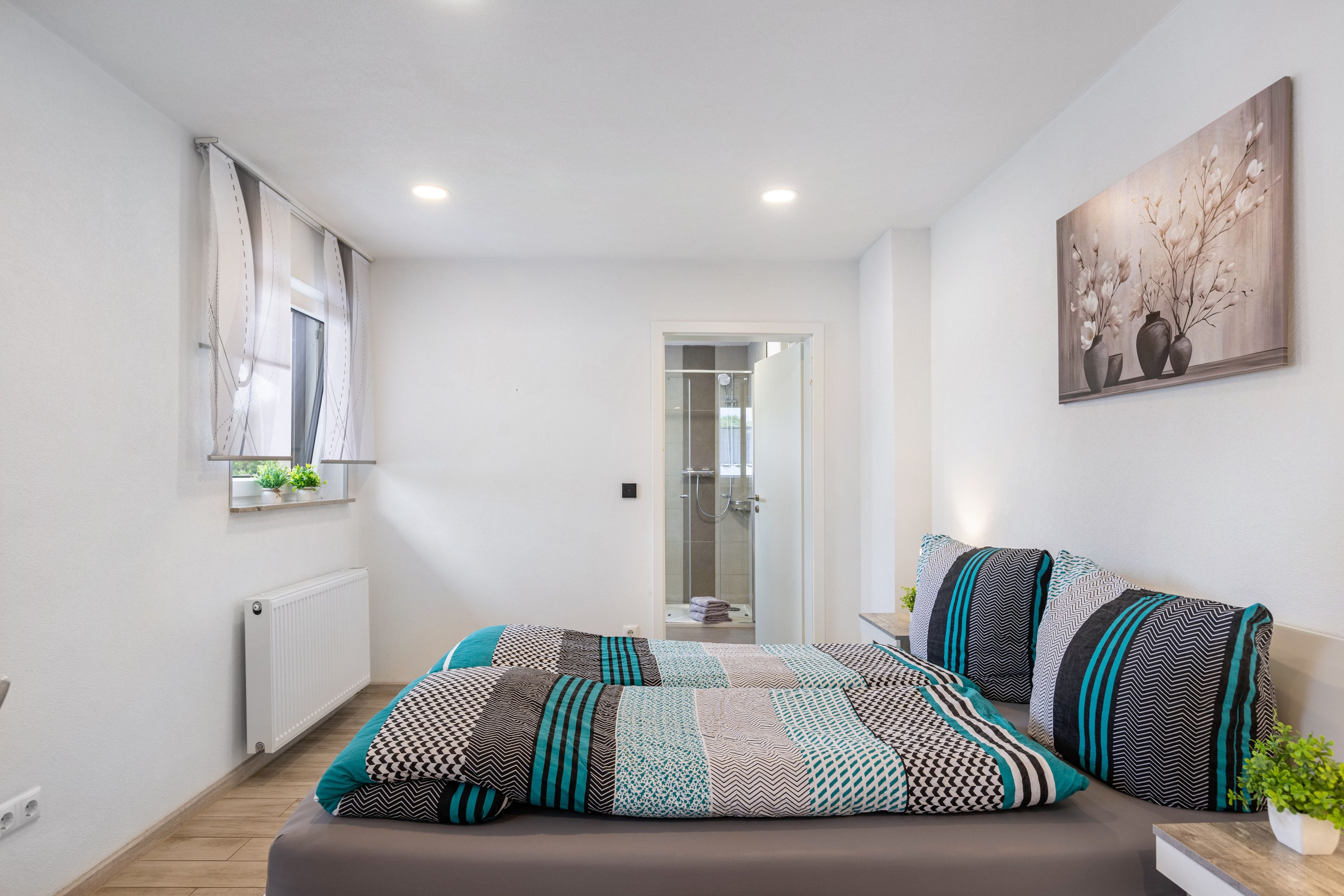 Ein modernes Schlafzimmer mit Bett, einem Fenster mit Vorhängen, einer Dusche und einem Bild an der Wand.