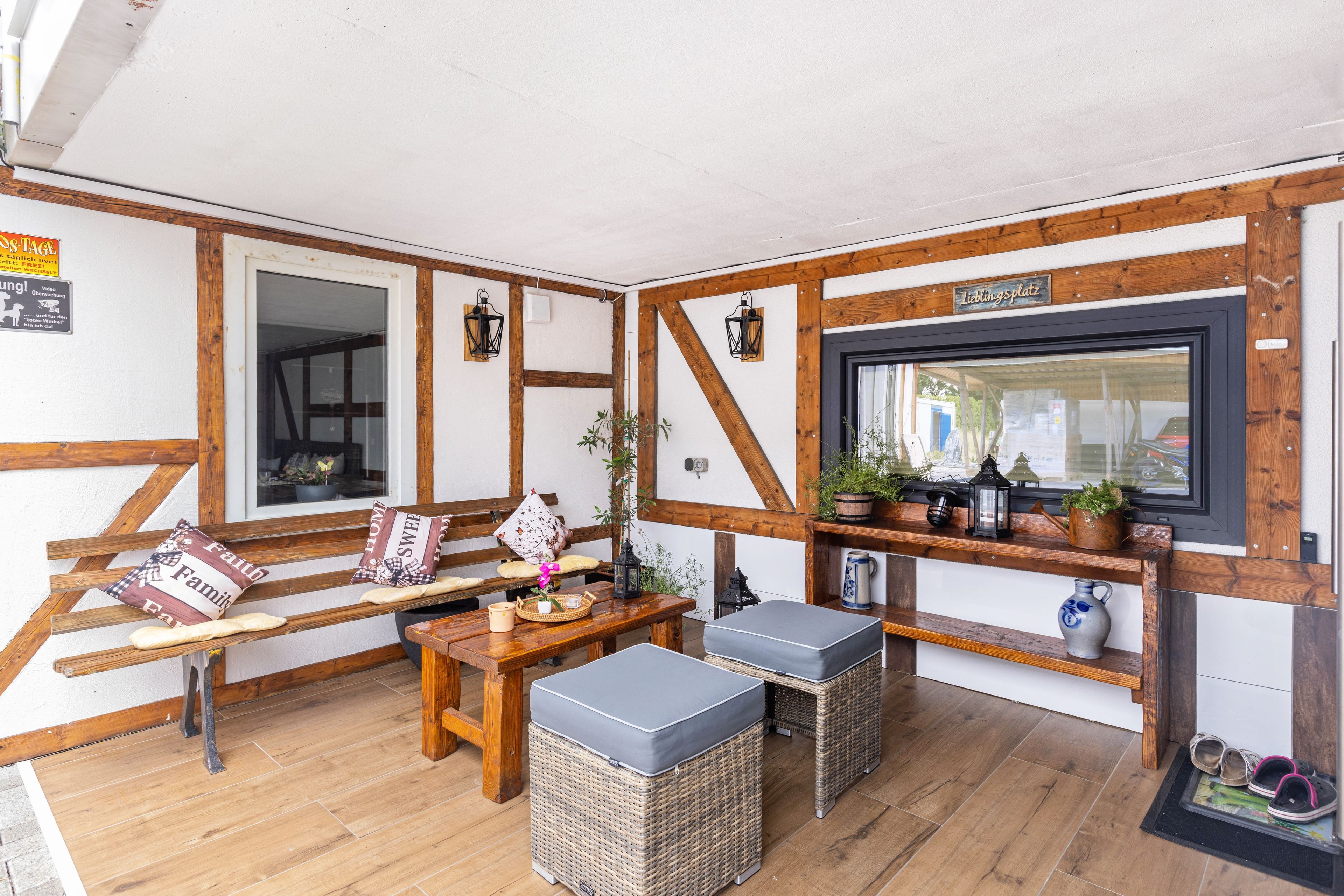 Ein gemütliches Zimmer mit einer hölzernen Bank, einem kleinen Tisch, Flechtpoufs und einem an der Wand montierten Fernseher.