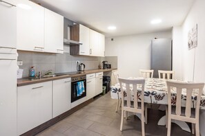 Ett modernt kök med vita skåp, en inbyggd ugn, en kaffebryggare och en matplats med ett bord och stolar.
