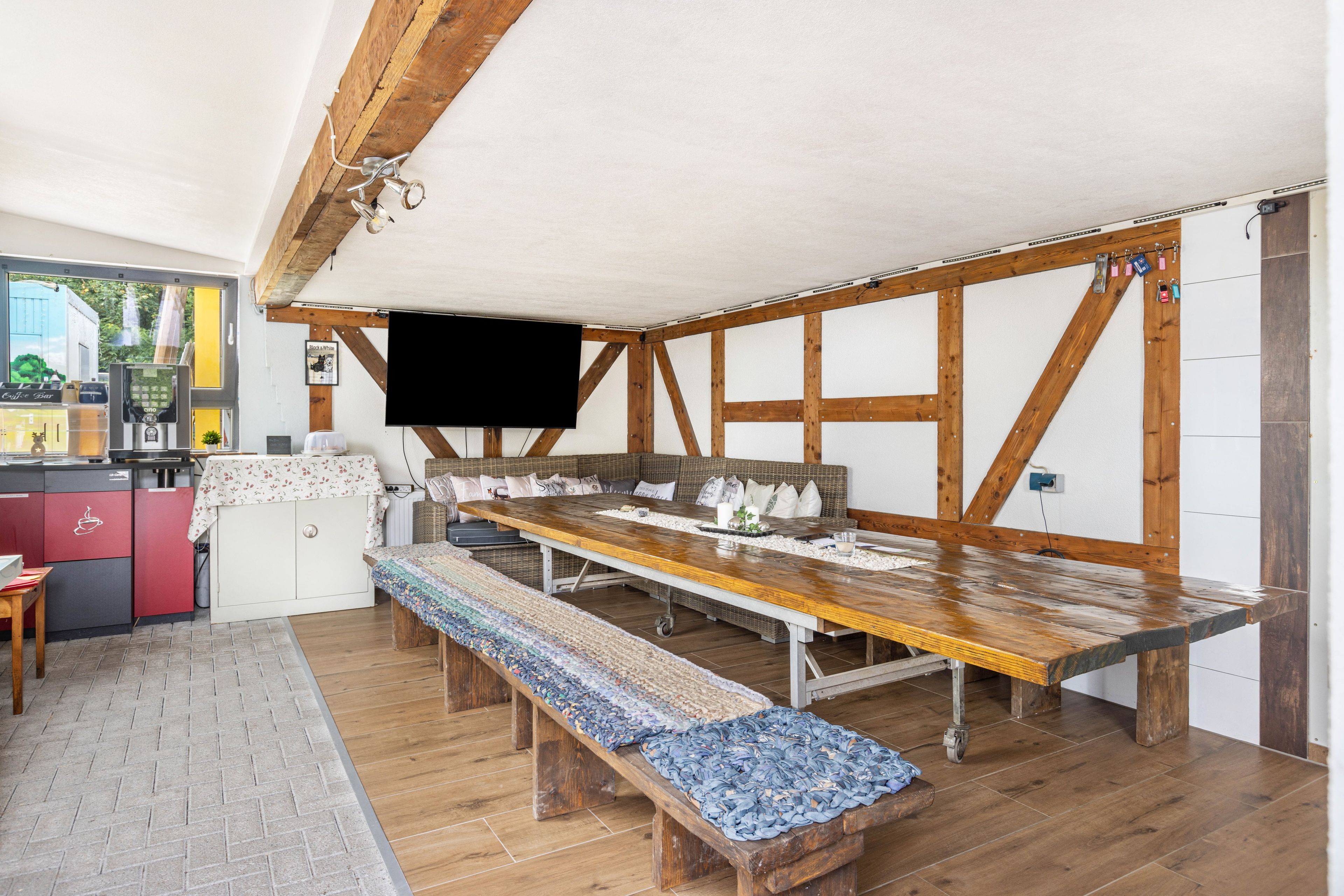 Ein Essbereich mit einem langen Holztisch, Bänken und einem an der Wand befestigten Fernseher.