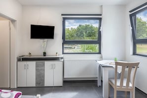 A modern kitchen with a built-in TV, a dining area with a table and chair, and a window with a view of greenery. - Room 'Einzelzimmer 9' with Shared Garden and Wi-Fi (Stadtallendorf)