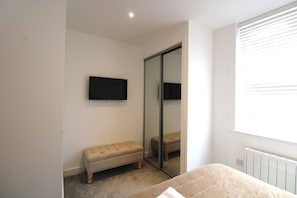 A bedroom with a bed, a bench, a television, and a sliding door. - Immaculate town center apartment with full kitchen and free parking (Basingstoke)