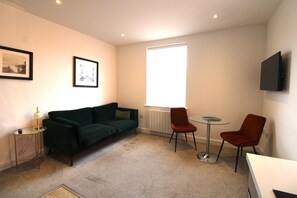 Quarto com um sofá verde, duas cadeiras vermelhas, uma mesa pequena e um abajur.