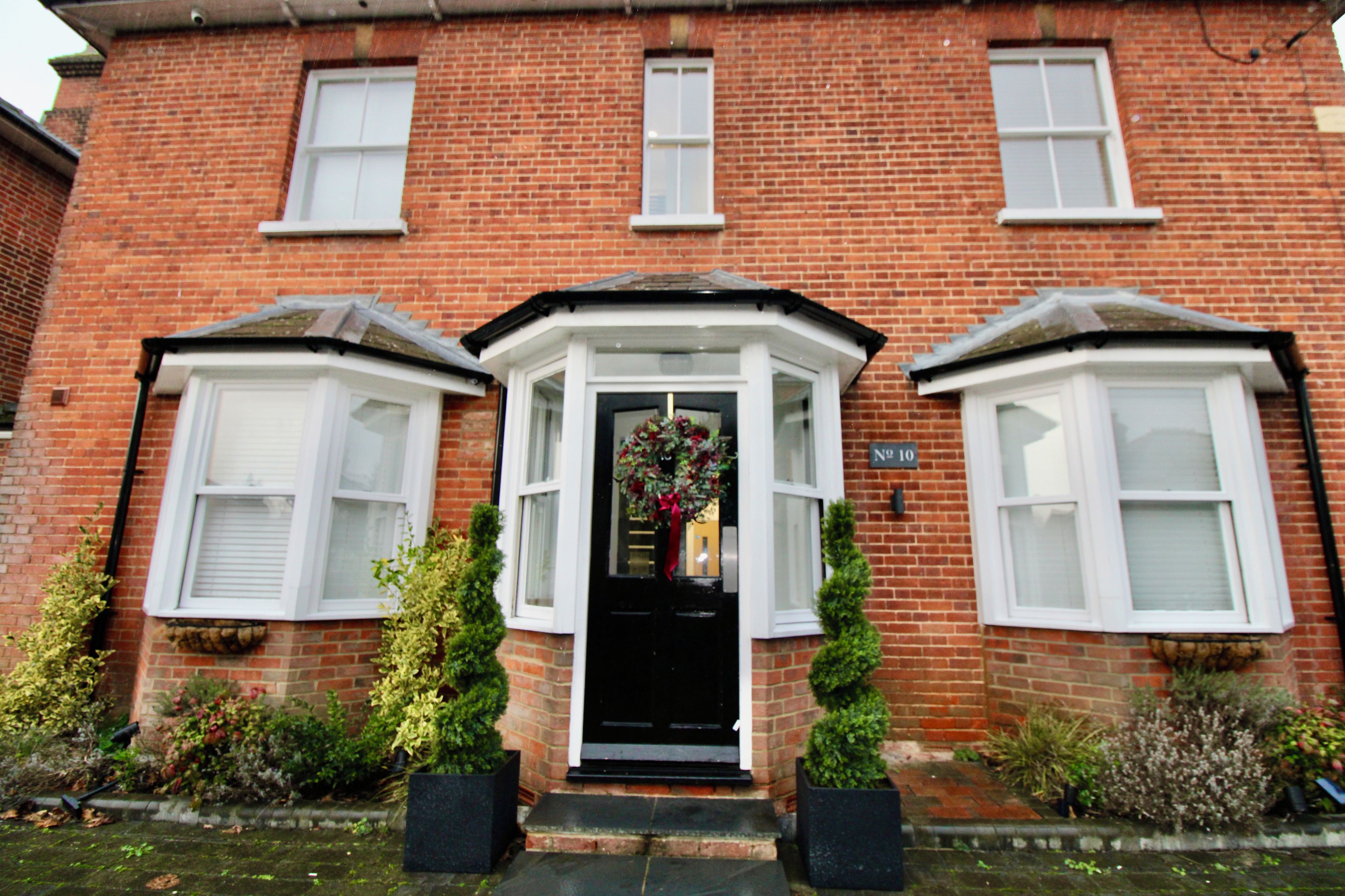 A red brick house with a black front door, white window frames, and a bay window on the left.