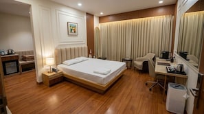 Ein Hotelzimmer mit Bett, Nachttisch, Lampe, Schreibtisch, Stuhl und einem großen Spiegel.