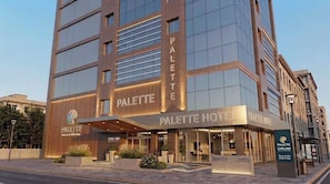 Um hotel com fachada moderna, grandes janelas e uma placa indicando ser o 'PALETTE HOTEL'.