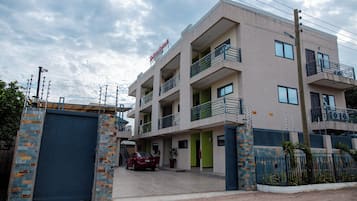 A multi-story building with a gated entrance, a red car parked in front, and a sign indicating a restaurant.