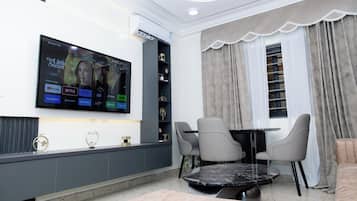 A modern living room with a flat-screen TV mounted on the wall, a dining table with chairs, and a sofa.