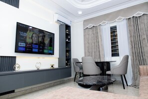 Een moderne woonkamer met een flatscreen televisie aan de muur, een eettafel met stoelen en een bank.