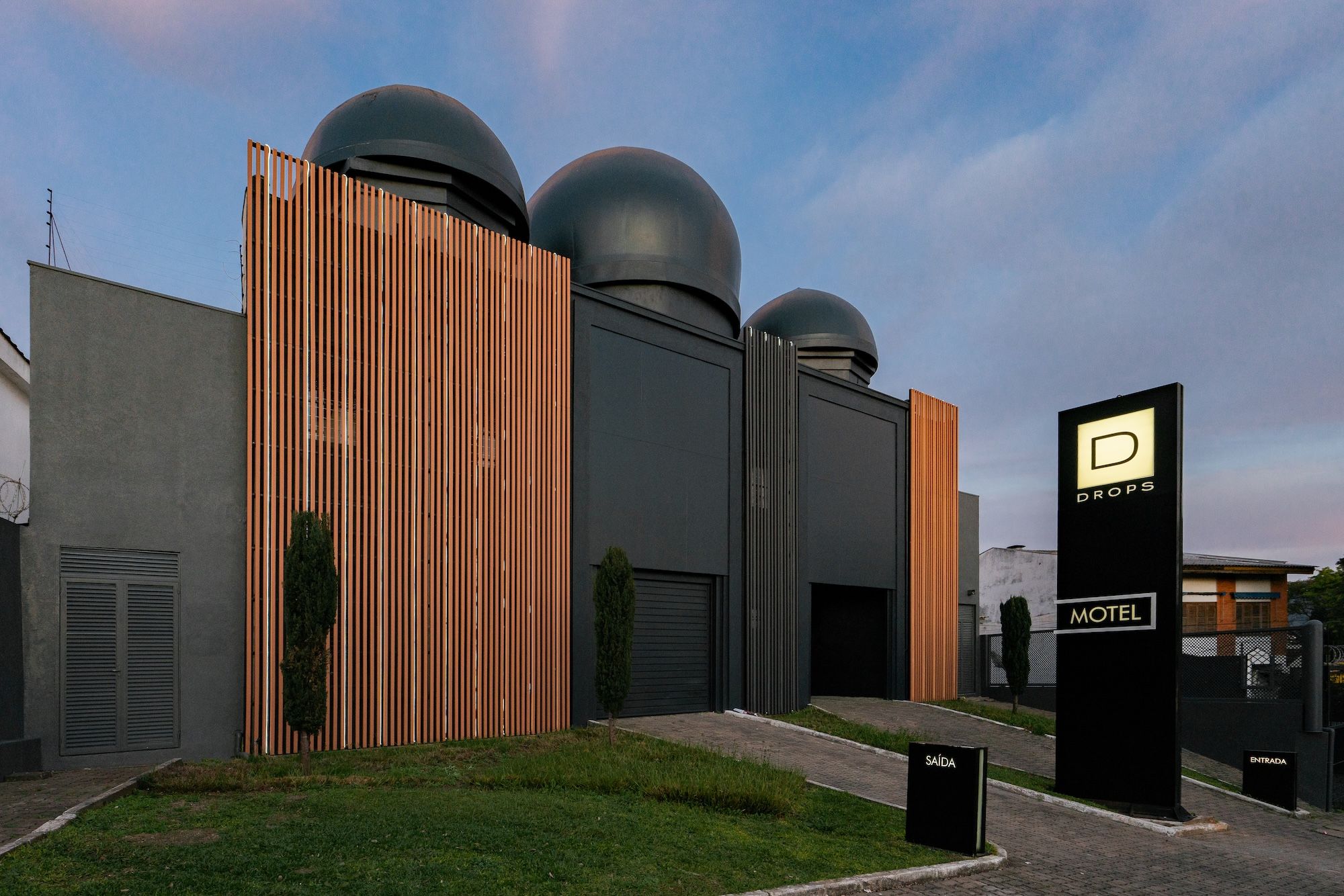 Un edificio moderno con un letrero llamativo para un motel, que presenta un diseño minimalista con listones verticales de madera y estructuras esféricas en la parte superior.