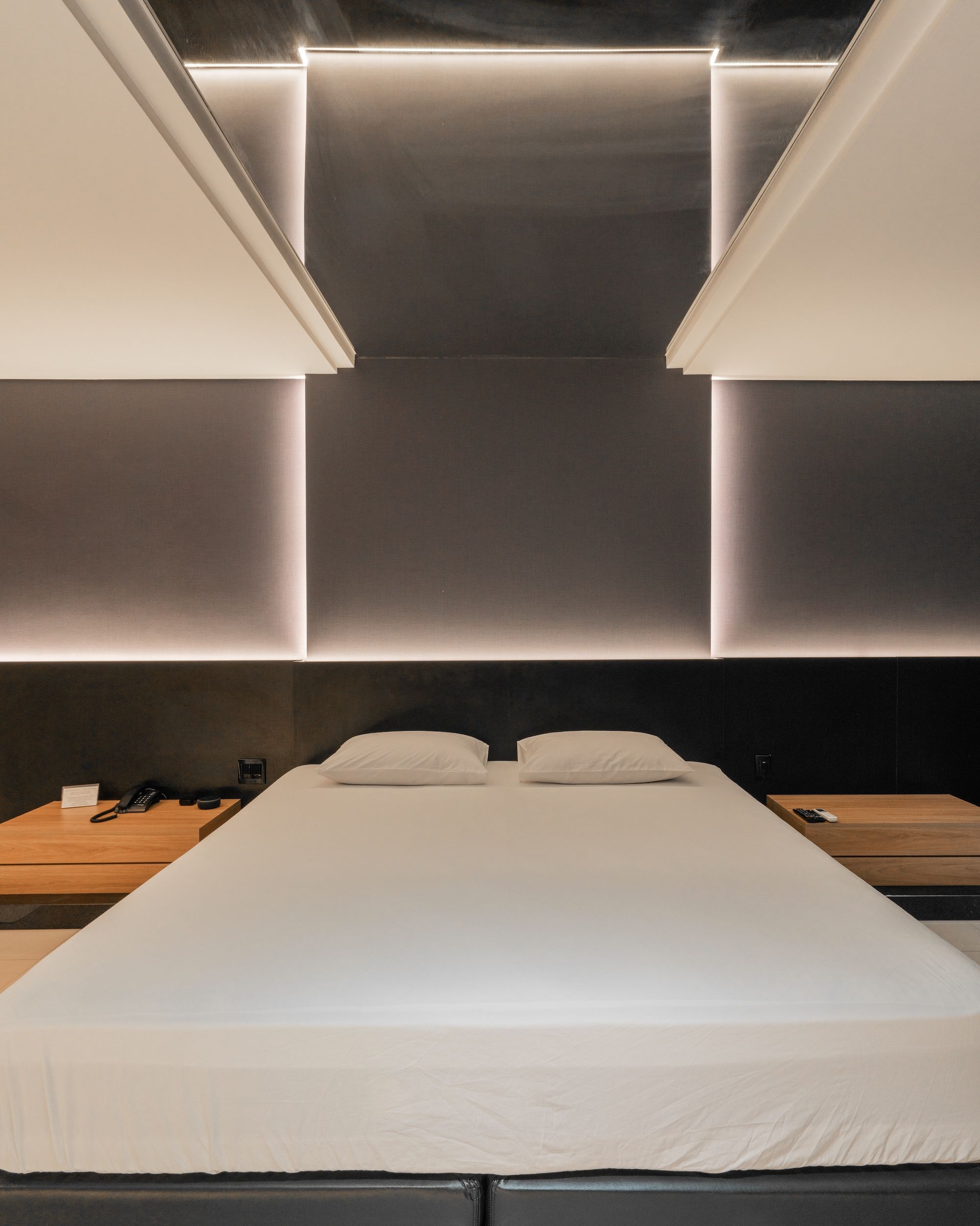 A modern hotel room with a large bed, bedside tables, a telephone, and a wooden nightstand.