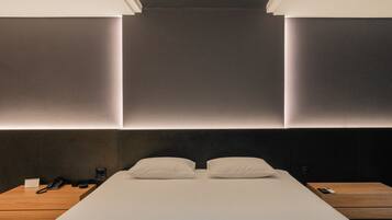 A modern hotel room with a large bed, bedside tables, a telephone, and a wooden nightstand.