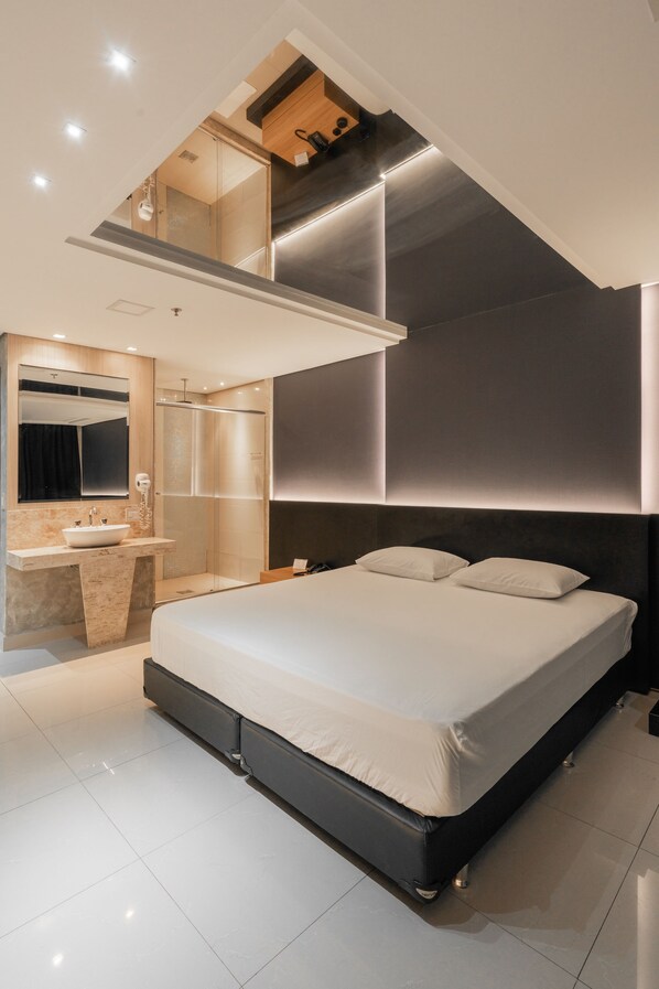 Un dormitorio moderno con una cama grande, un escritorio empotrado y zona de ducha.