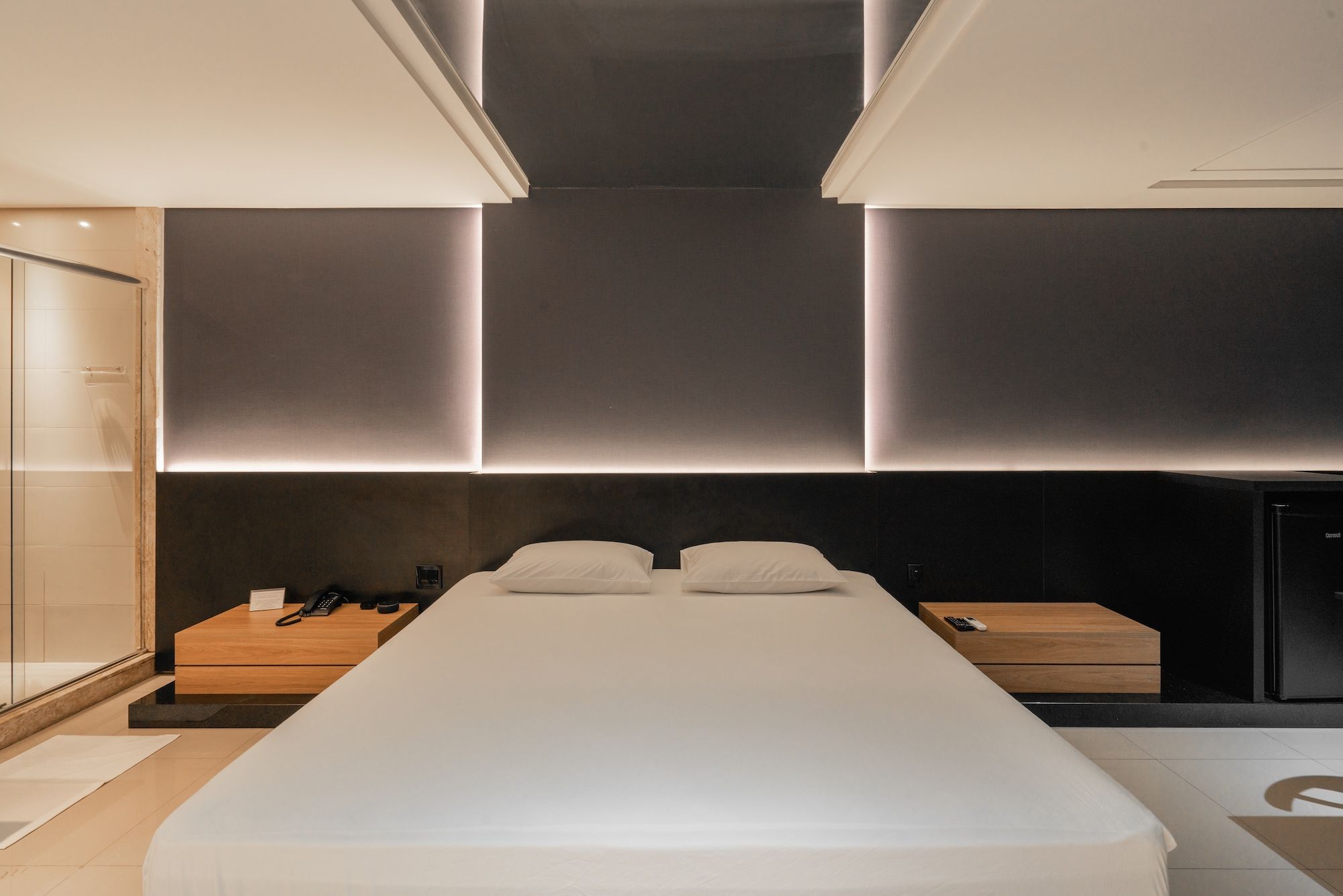 A modern hotel room with a large bed, bedside tables, a wardrobe, and a built-in bench.