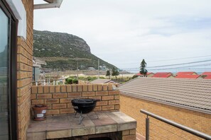 A balcony with a barbecue grill, a potted plant, and a view of a mountain and houses in the background. - The Place of Grace - North Shore (Cape Town)