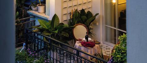 A balcony with potted plants, a wicker chair, and string lights.