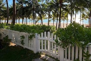 A white picket fence leading to a beach with palm trees and a clear view of the ocean. - Luxury Private Pool Beachfront Villa - My Khe Beach Danang (Ngu Hanh Son)