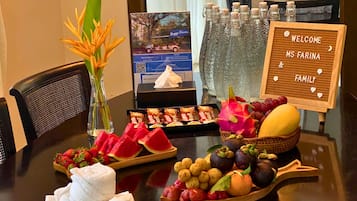 A table with a welcome sign, snacks, fruits, and a vase with flowers.
