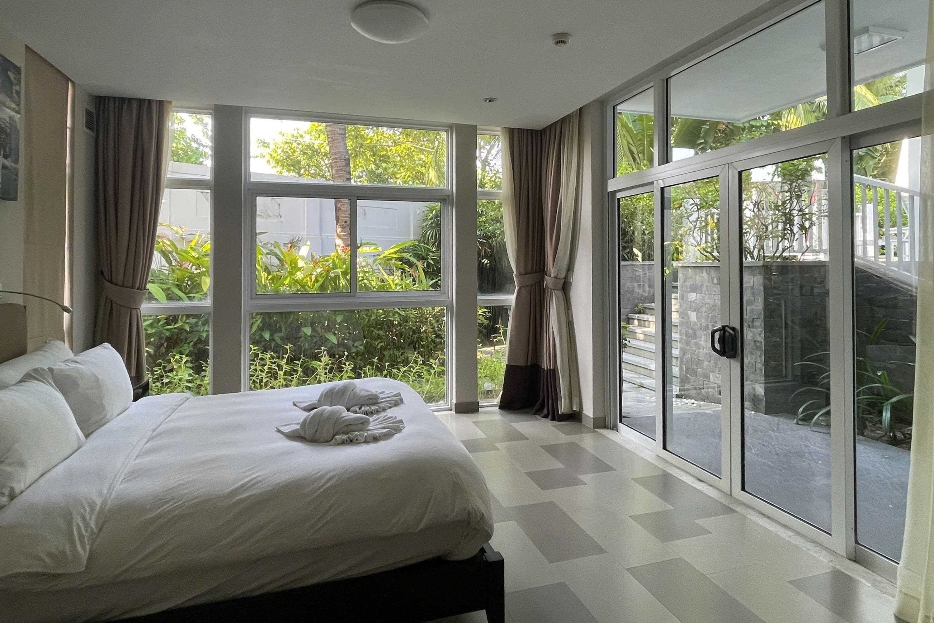 Un dormitorio con una cama grande, vistas a zonas verdes y una puerta corrediza de vidrio.