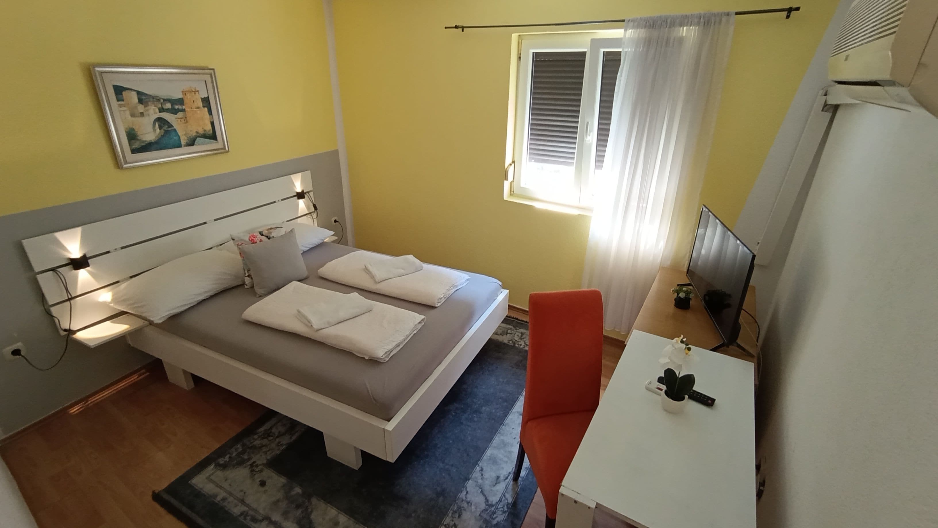 Una stanza con un letto, una scrivania, una sedia, una televisione e una finestra con tende.