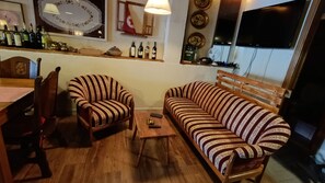 Una sala de estar con un sofá de madera, un sillón a rayas, una mesa de centro de madera y una zona de comedor con una mesa y sillas de madera.