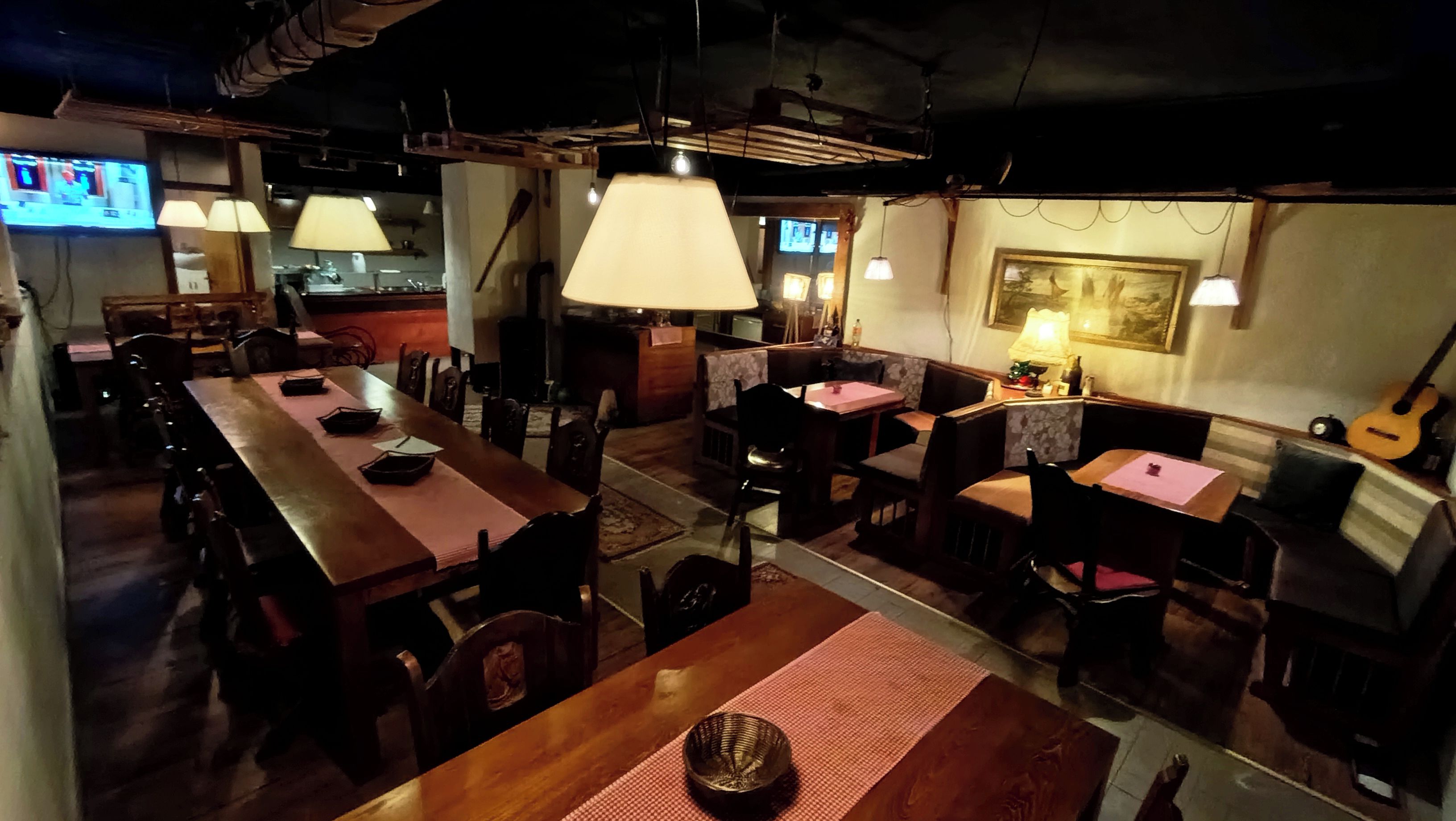 Un ristorante con tavoli e sedie di legno, lampade a sospensione e una chitarra appesa al muro.