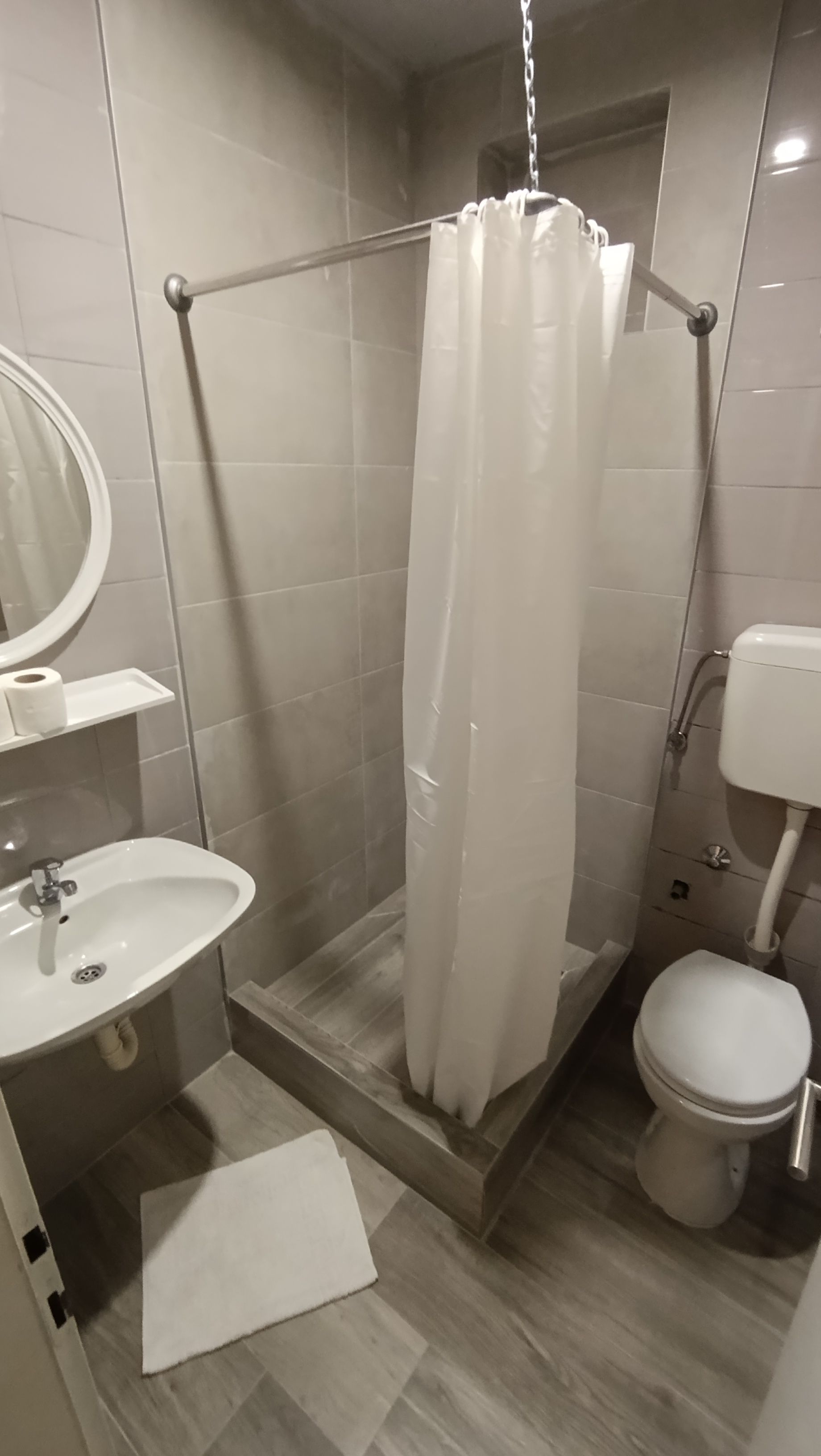 A bathroom with a shower, toilet, sink, and a mirror.