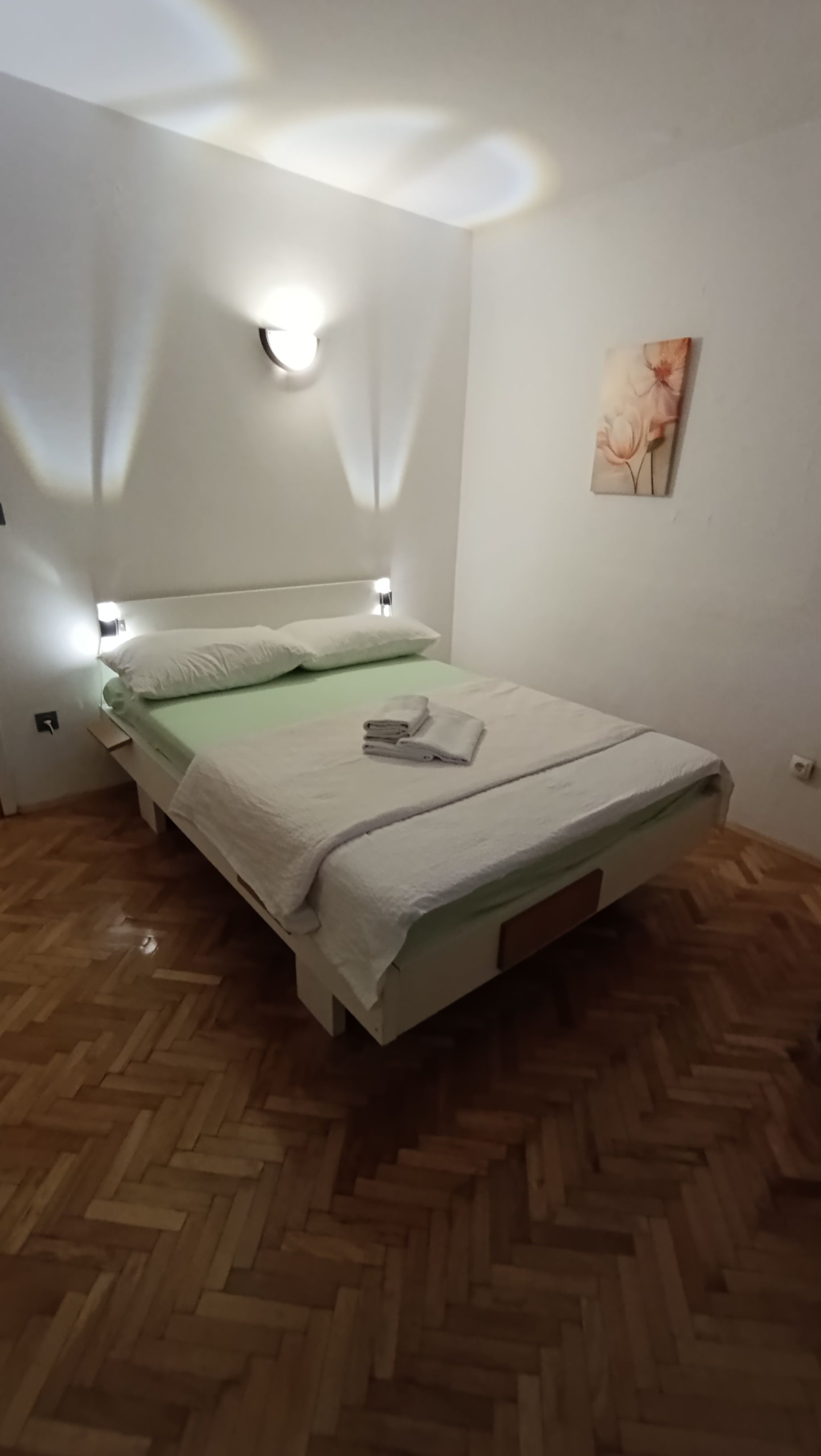 A room with a bed, a wall-mounted light, and a painting.