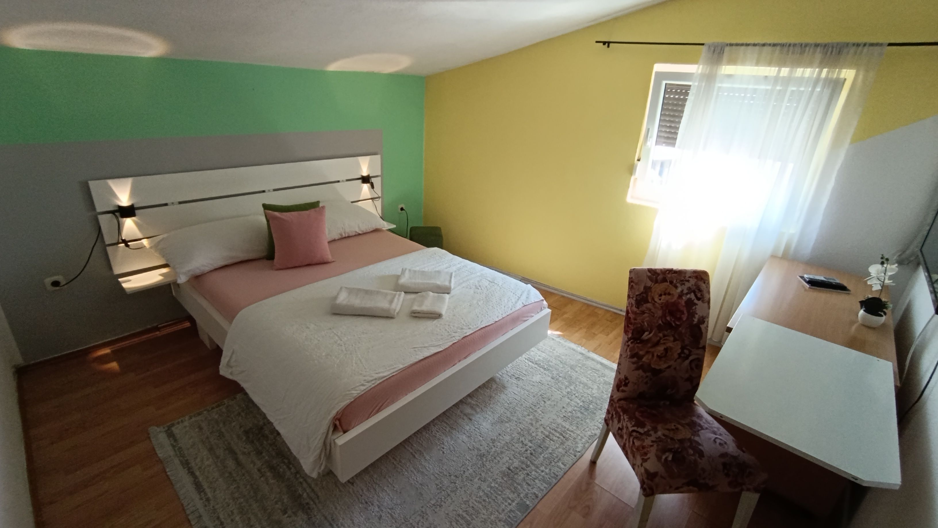 Habitación de hotel con cama, mesita de noche, silla y ventana con cortinas.