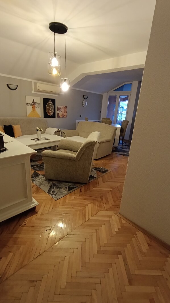 A living room with a herringbone wooden floor, a white sofa, a beige armchair, and a coffee table.