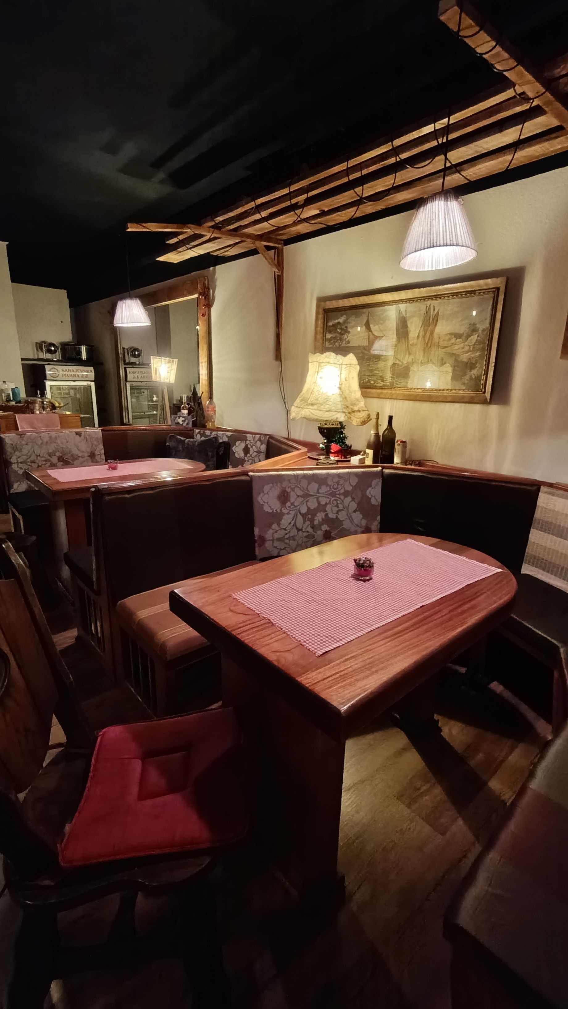 Un interior de restaurante con mesas y cabinas de madera, una lámpara colgante y un cuadro enmarcado en la pared.