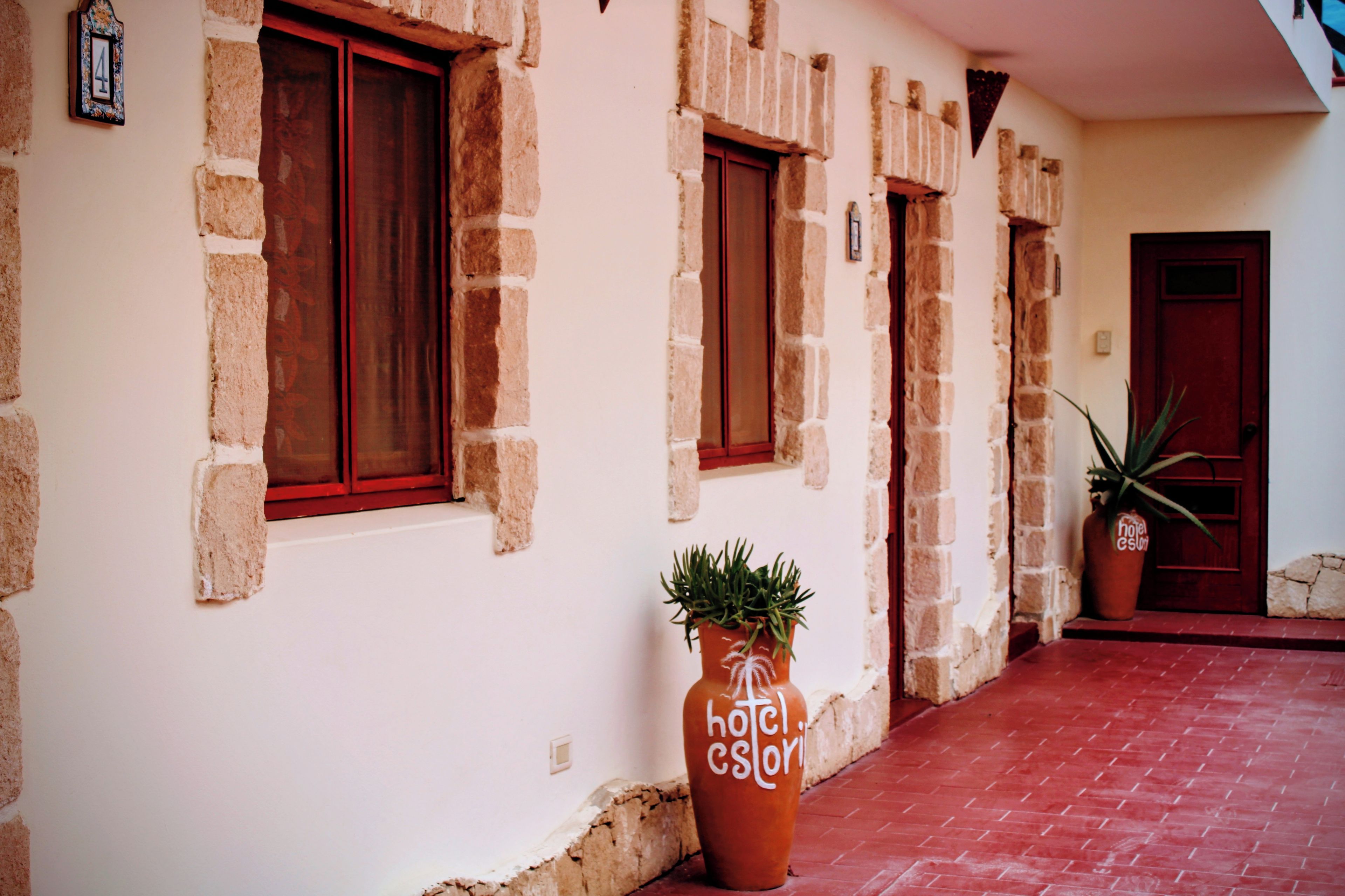A building with stone walls and red-framed windows, a potted plant, and a red door.