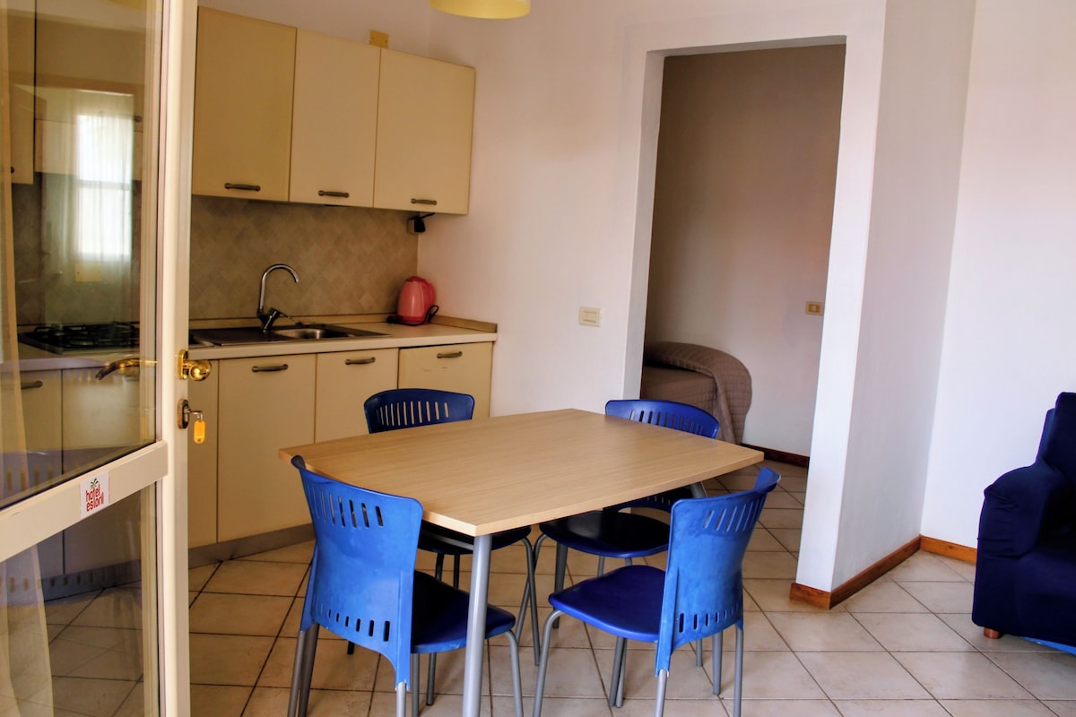 Una cocina compacta con una mesa de comedor y sillas, una tetera roja y una estufa.