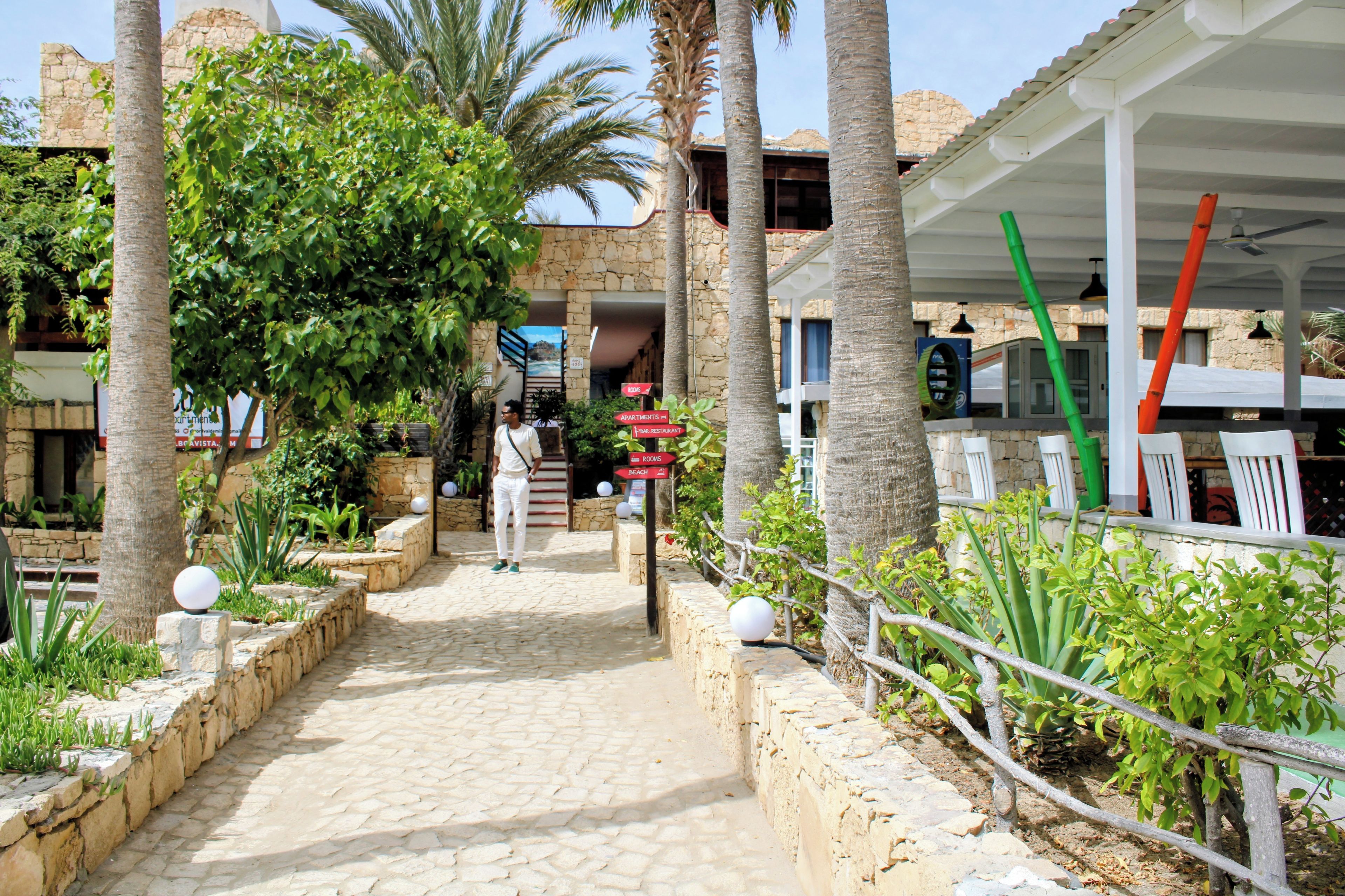 A stone pathway leading to a building with a sign indicating rooms, apartments, and a bar/restaurant.