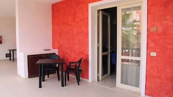 Una habitación con una pared roja, puerta corredera de vidrio, una mesita con dos sillas y un techo blanco.