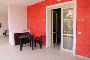 Una habitación con una pared roja, puerta corredera de vidrio, una mesita con dos sillas y un techo blanco.