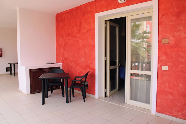 A room with a red wall, a sliding glass door, a small table with two chairs, and a white ceiling.