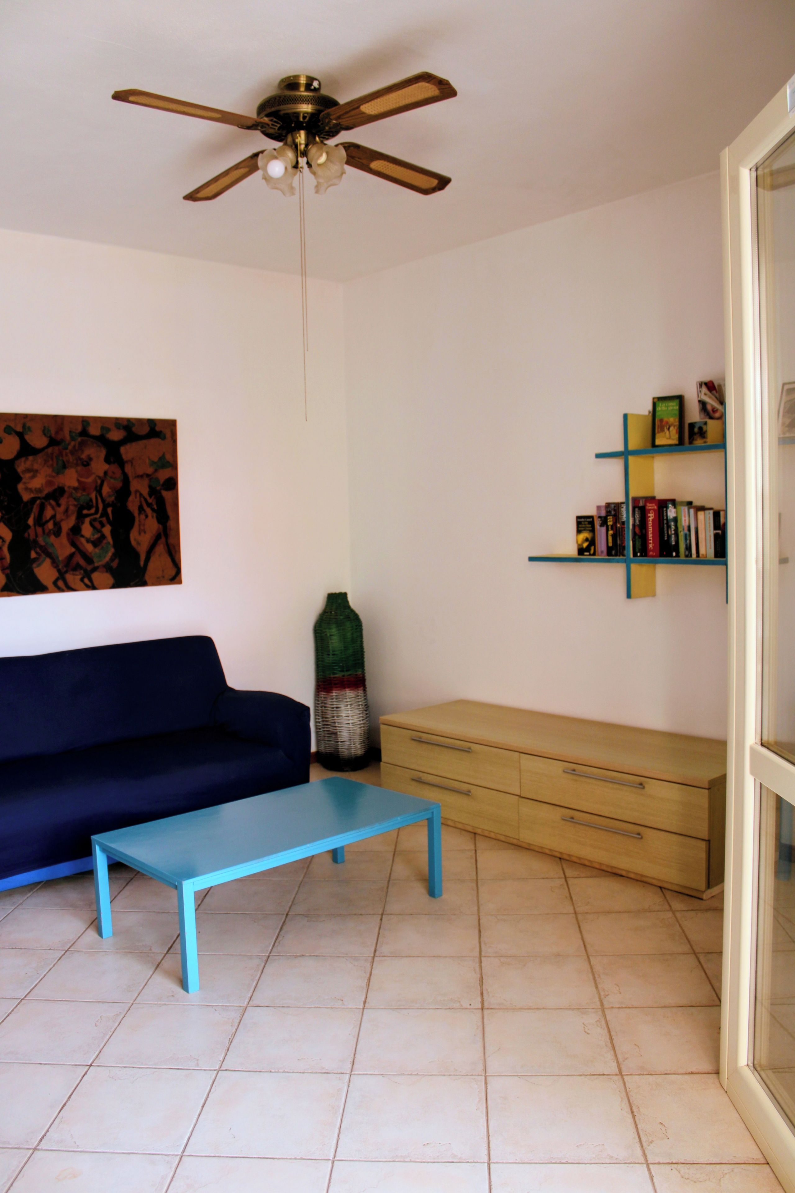 Ein Wohnzimmer mit einem blauen Sofa, einem Couchtisch, einem Bücherregal und einem Deckenventilator.