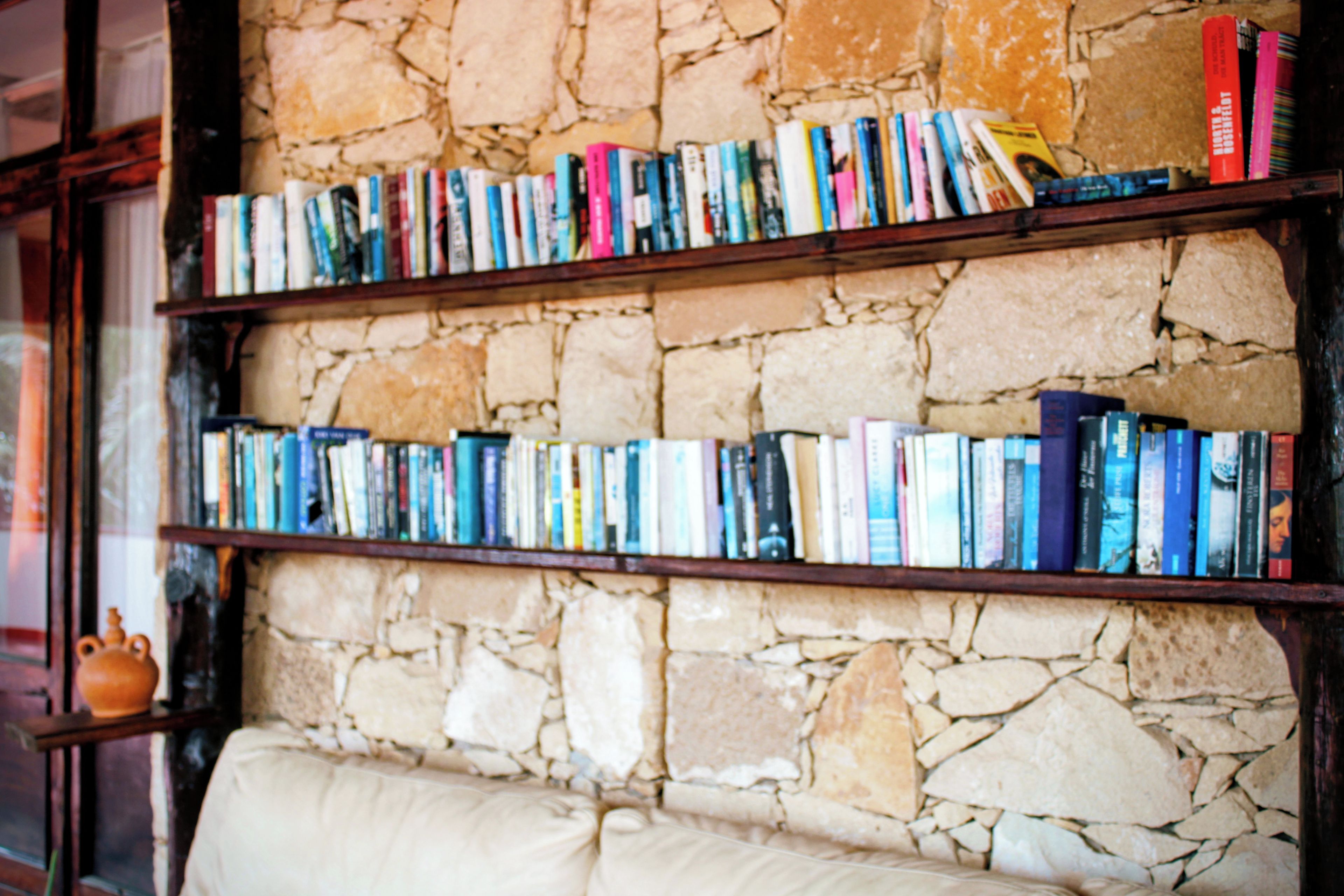 Una estantería llena de libros frente a una pared de piedra.