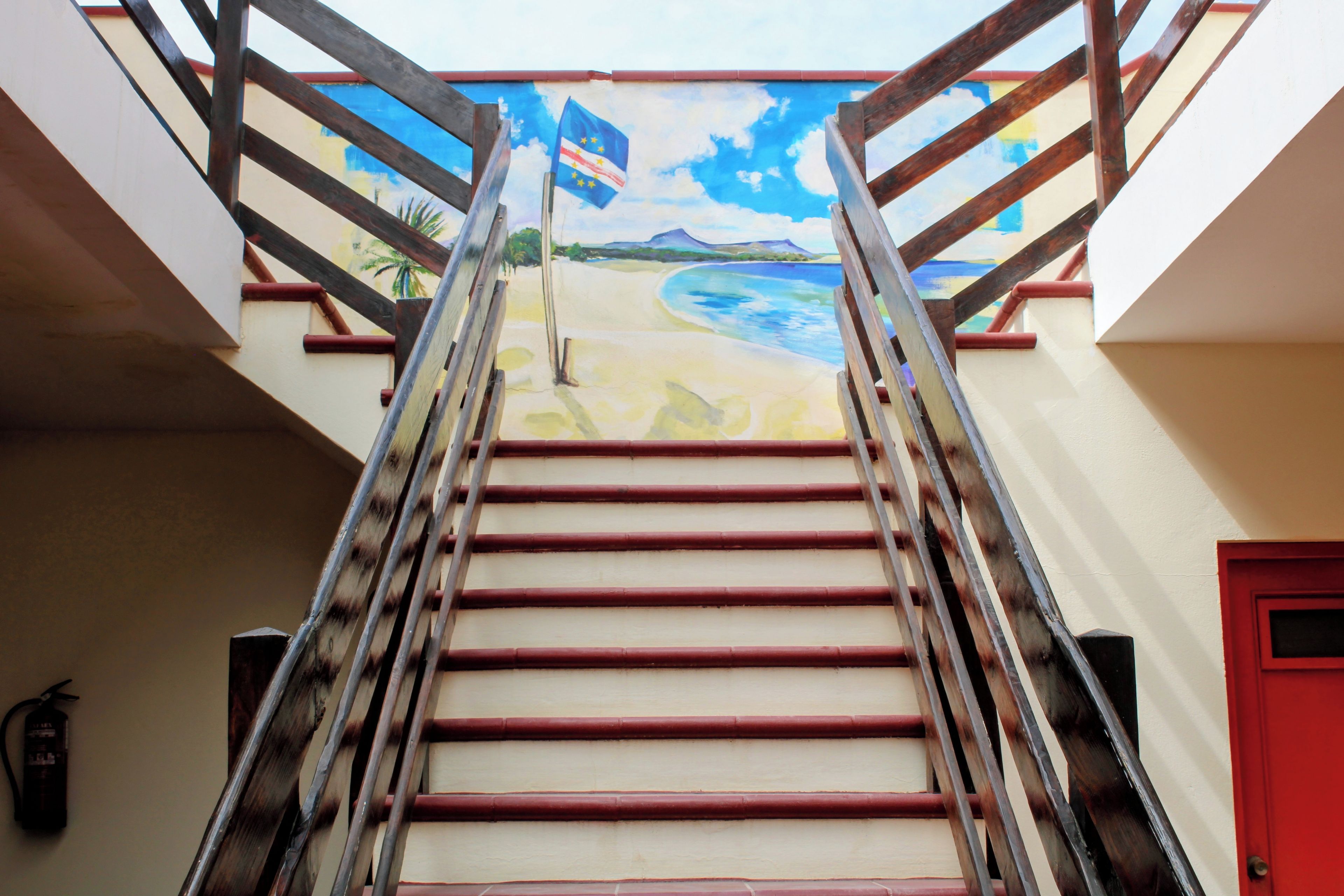 A staircase with a handrail leading to a landing with a red door.