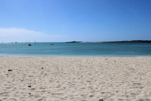 A sandy beach with calm waters and boats in the distance.
