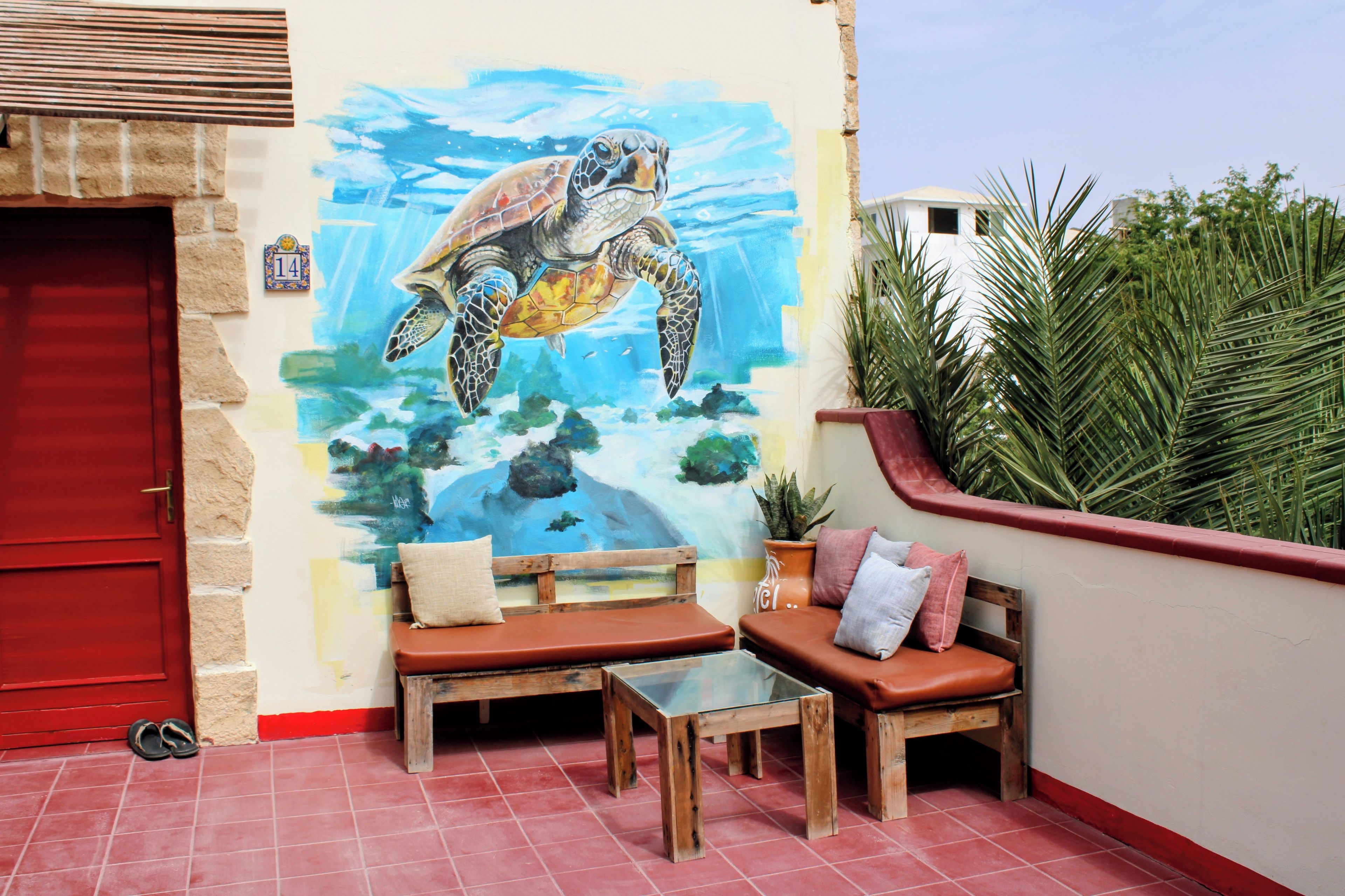 A room with a mural of a sea turtle, a red door, a bench, a table, and a potted plant.