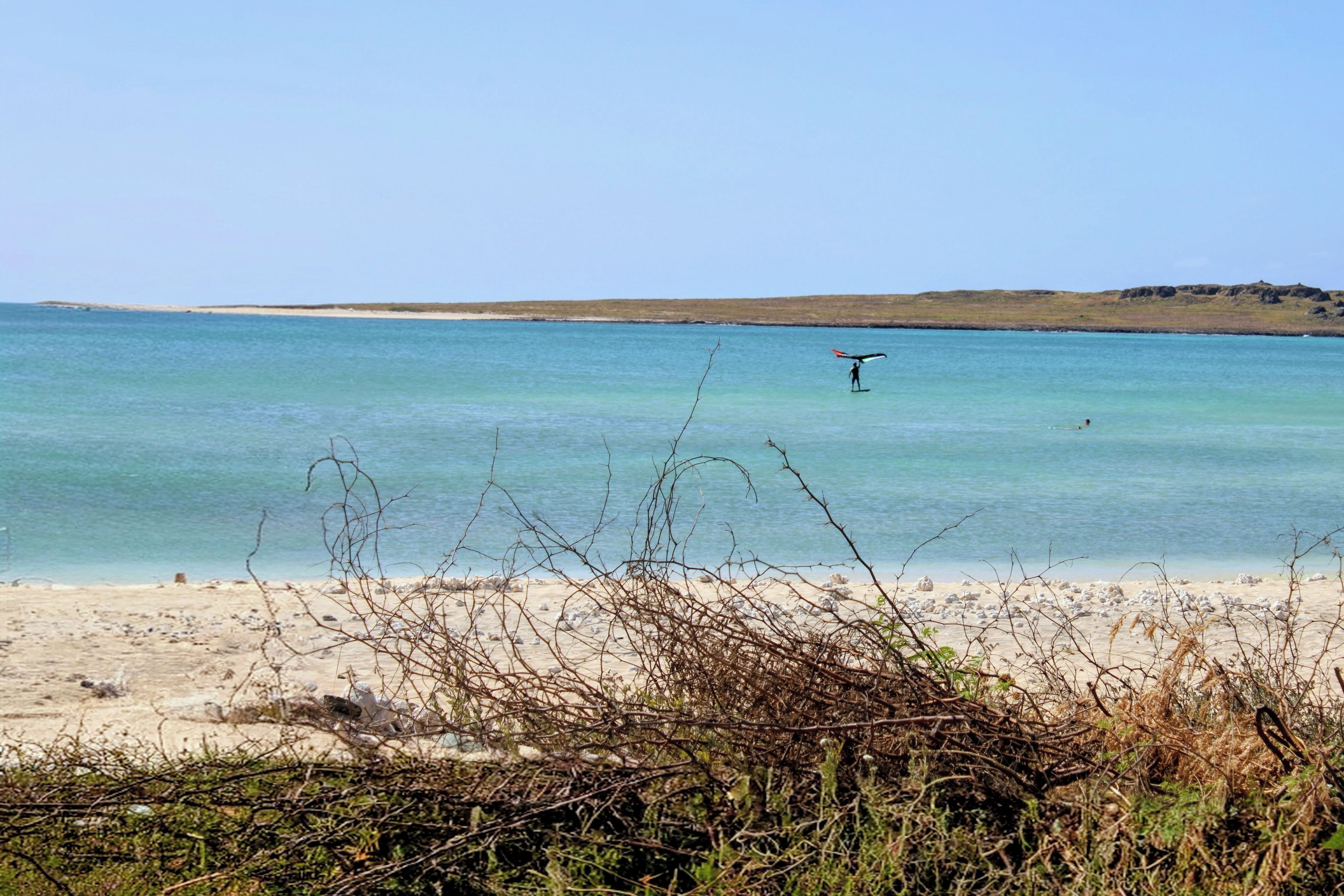 A beach with clear turquoise water, a sandy shore, and sparse vegetation in the foreground.